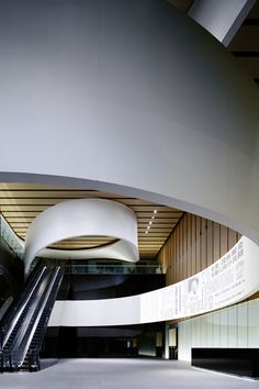 an escalator in front of a large white building with curved walls and stairs