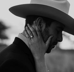 a man in a cowboy hat holding his hand to his face