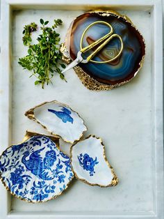 some blue and white dishes with scissors on them next to herbs in a tray that has gold trimmings