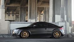 a black sports car parked in front of a building with gold rims on it