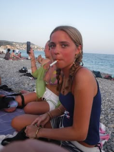 two young women sitting on the beach with their cell phones in their mouths and one woman holding her hand up to her mouth