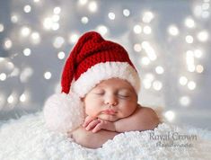 a baby wearing a santa hat sleeping on top of a white blanket with lights in the background