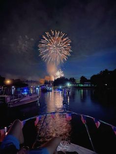 fireworks are lit up in the night sky over water with boats and people watching them