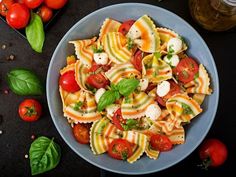 a blue bowl filled with pasta and tomatoes next to some fresh basil on the side