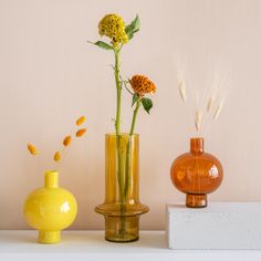 three vases with flowers in them sitting on a white shelf next to each other