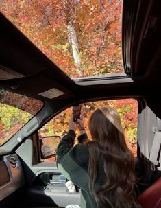 a woman sitting in the driver's seat of a car looking at fall foliage