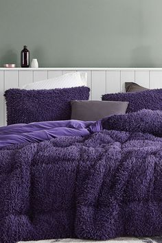 a bed with purple comforter and pillows on it