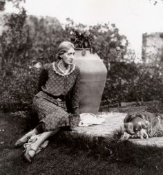 an old black and white photo of a woman sitting next to a vase with a dog laying on the ground