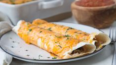 two burritos on a white plate with a bowl of salsa in the background