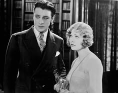 an old black and white photo of a man in a suit and tie standing next to a woman