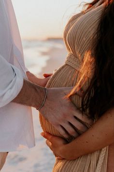 a pregnant woman holding her husband's hand on the beach