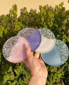 hand holding three different colored coasters in front of bushes