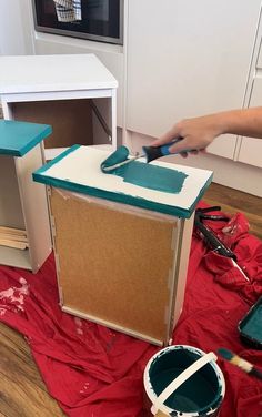 a person is painting a cabinet in the middle of a room with red tarp