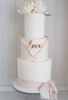 a three tiered wedding cake with white flowers on the top and love written on the side