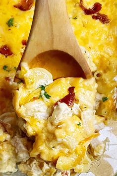 a wooden spoon scooping out some food from a casserole dish with cheese and bacon