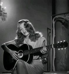 a woman is playing an acoustic guitar in a room with chandeliers on the wall