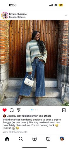 a woman is standing outside with her hand on her hip, wearing jeans and a sweater