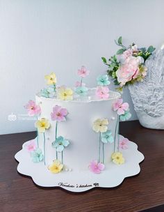 a white cake with flowers on it sitting on top of a table next to a vase