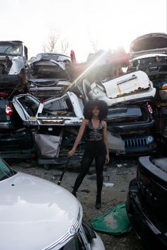 a woman standing in front of a pile of junk next to a white car with the hood up