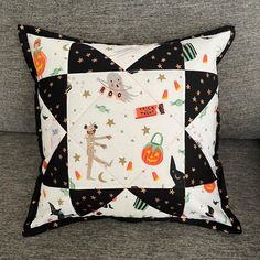 a black and white patchwork pillow on a gray couch with an orange pumpkin design