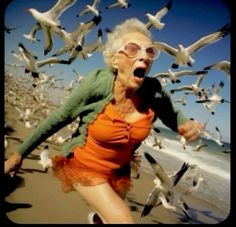 an old woman running on the beach with seagulls flying around her