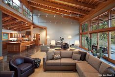 a living room filled with lots of furniture next to large windows and wooden ceiling beams