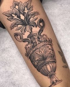 a black and white tattoo on the leg of a woman's arm with an ornate vase