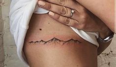 a woman's stomach with a small mountain tattoo on her left side ribcage