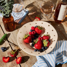 strawberries and blueberries in a white bowl on a wooden table next to bottles of wine