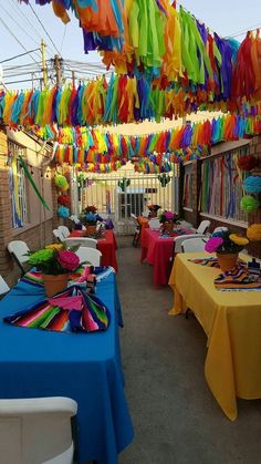 an outdoor party with colorful streamers hanging from the ceiling and tables covered in blue cloths