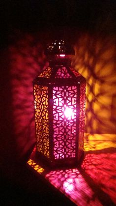 a lit lantern sitting on top of a table in front of a shadow filled wall