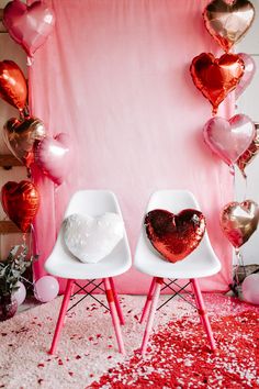 two white chairs with heart shaped pillows on them in front of a pink backdrop and balloons