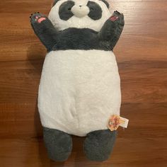 a stuffed panda bear laying on top of a wooden floor with its arms in the air