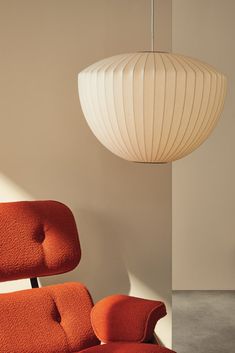 an orange chair sitting in front of a white light hanging from a ceiling fixture above it