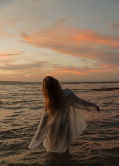 a woman standing in the ocean at sunset