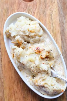 mashed potatoes and gravy in a white bowl on a wooden table with a spoon