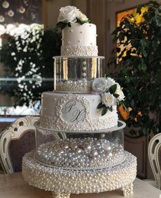 a three tiered wedding cake with pearls and flowers on top is displayed in front of a table