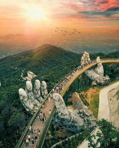 an aerial view of people walking on a bridge in the middle of mountains with birds flying overhead