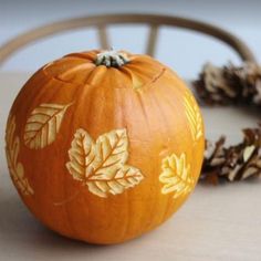 an orange painted pumpkin sitting on top of a table next to pine cones and a wooden chair