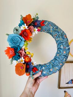 a person holding up a wreath made out of fabric and felt flowers on a wall