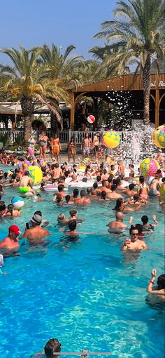 a large group of people are in the pool playing with water and beach balls while others watch