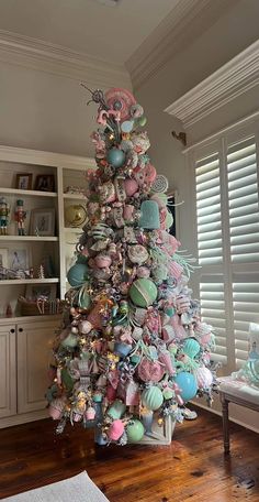 a decorated christmas tree in the corner of a room with white shutters and wooden floors