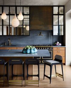 a kitchen with an island and stools next to the counter top, surrounded by hanging lights