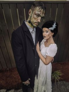 a man and woman dressed up as zombies standing next to each other in front of a wooden fence