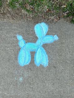 a blue teddy bear drawn in chalk on the ground next to some grass and dirt