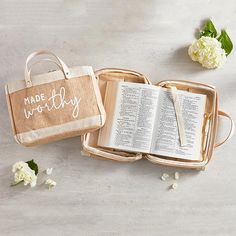 an open book with the word made worthy written on it next to a bag and flowers