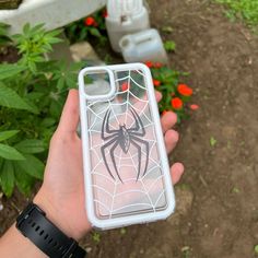 a person holding up an iphone case with a spider on it in front of some flowers