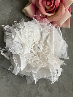 two pieces of white lace and a pink rose on a gray surface with grey background