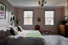 a bed room with a neatly made bed next to two windows and a chandelier