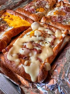 two pieces of bread with cheese and meat on it sitting on tin foil covered table